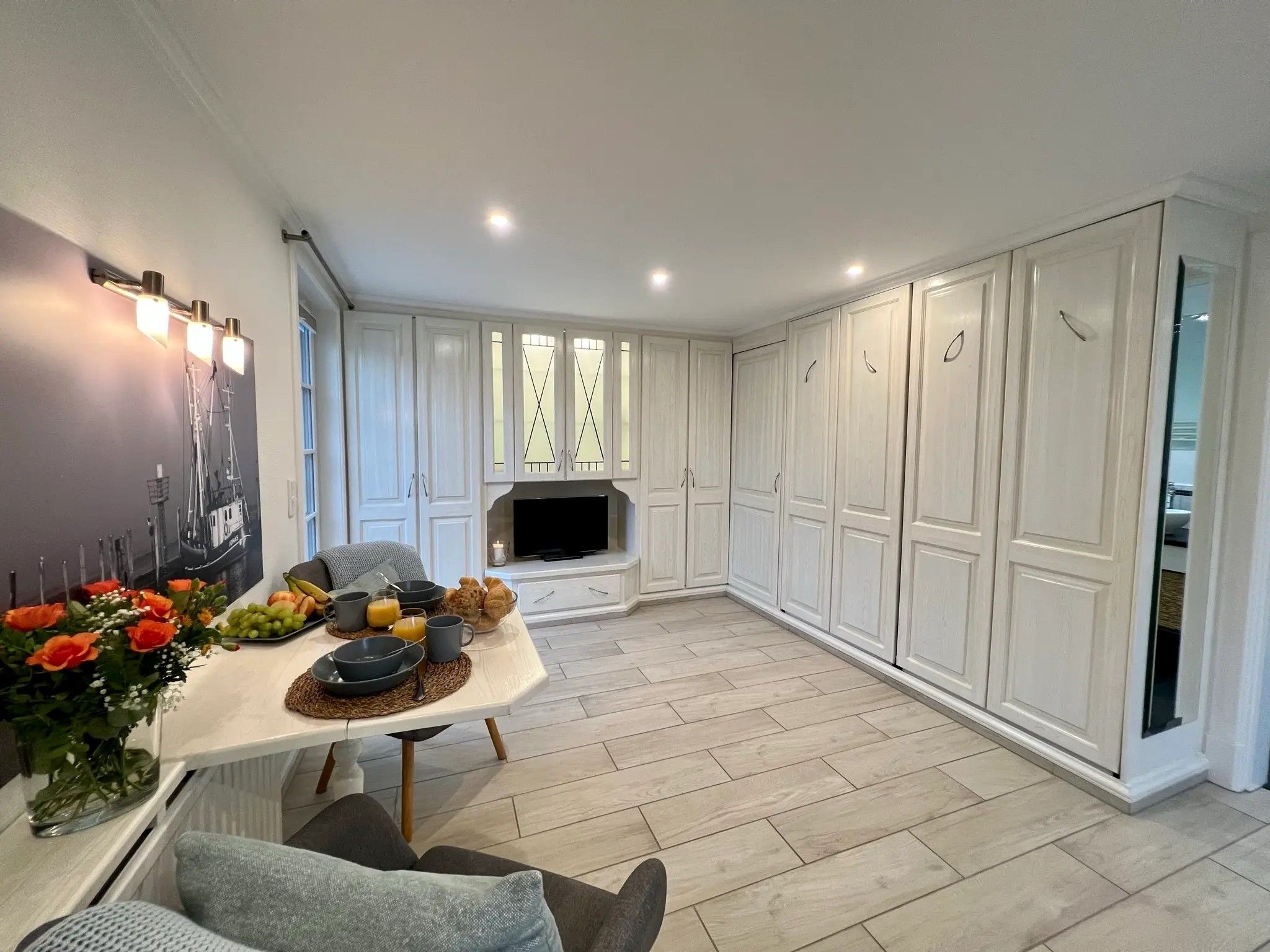 A modern kitchen with white cabinetry, a dining table set with breakfast items, and a flat-screen TV.