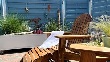 A wooden outdoor seating area with a chair and table, surrounded by plants and decorative items.
