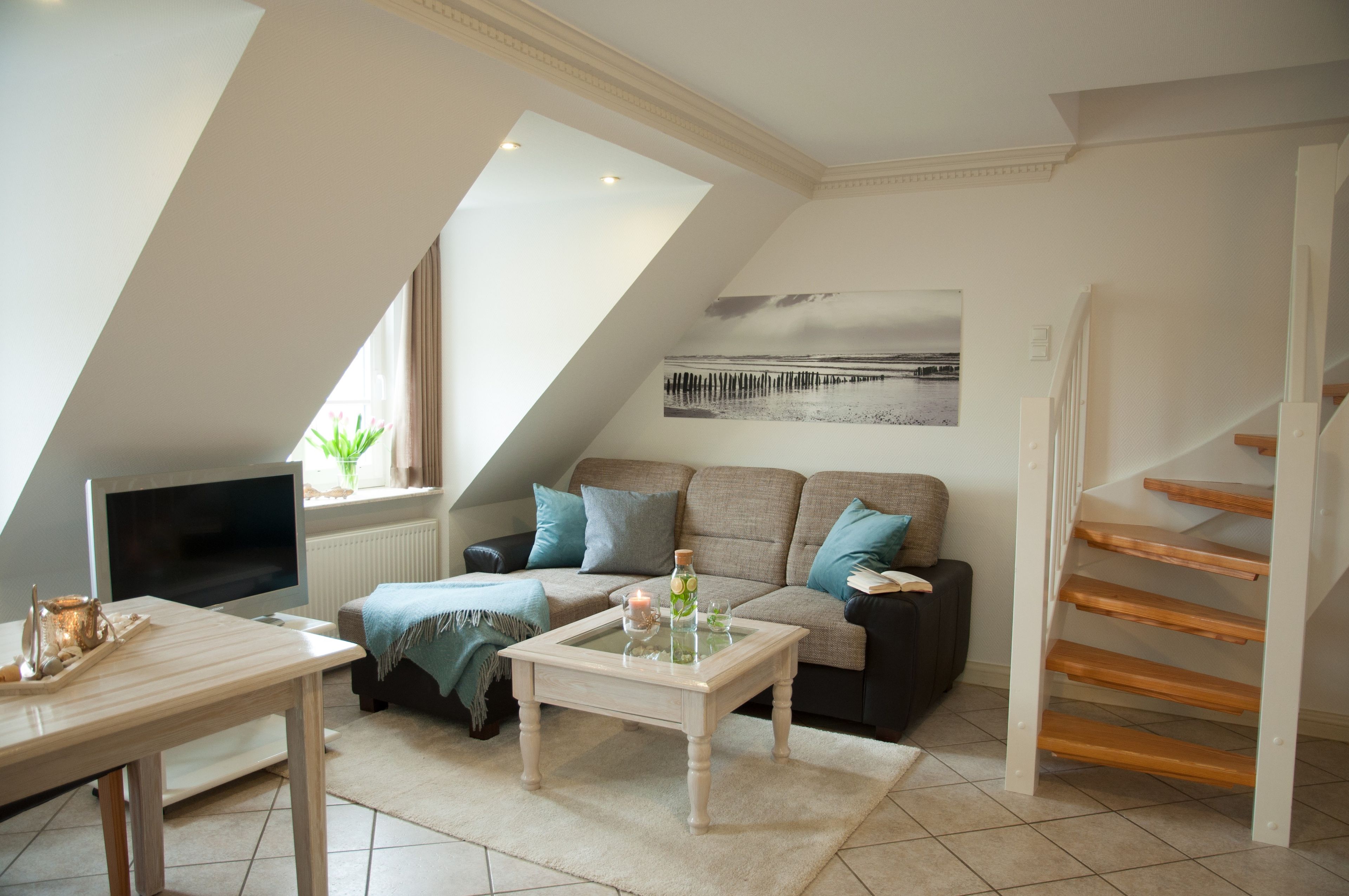 A modern living room with a sloped ceiling, a sofa, a coffee table, a TV, and a staircase.