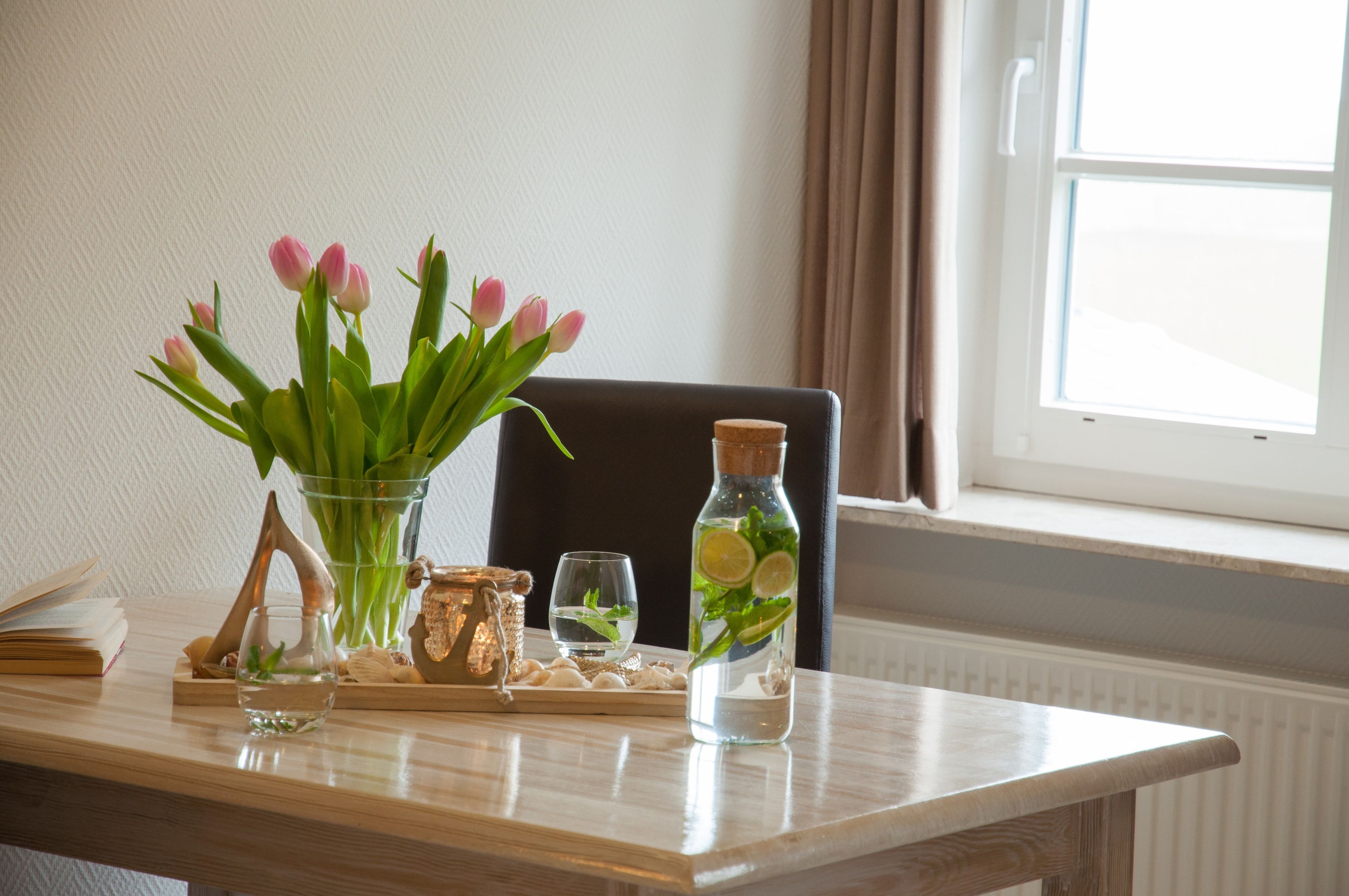 A table with a vase of pink tulips, a glass bottle with lime slices, and a small decorative item.