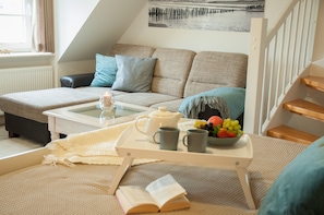 Ein gemütliches Wohnzimmer mit einer Couch, einem Couchtisch und einer Platte mit Teekanne, Tassen und Obst.