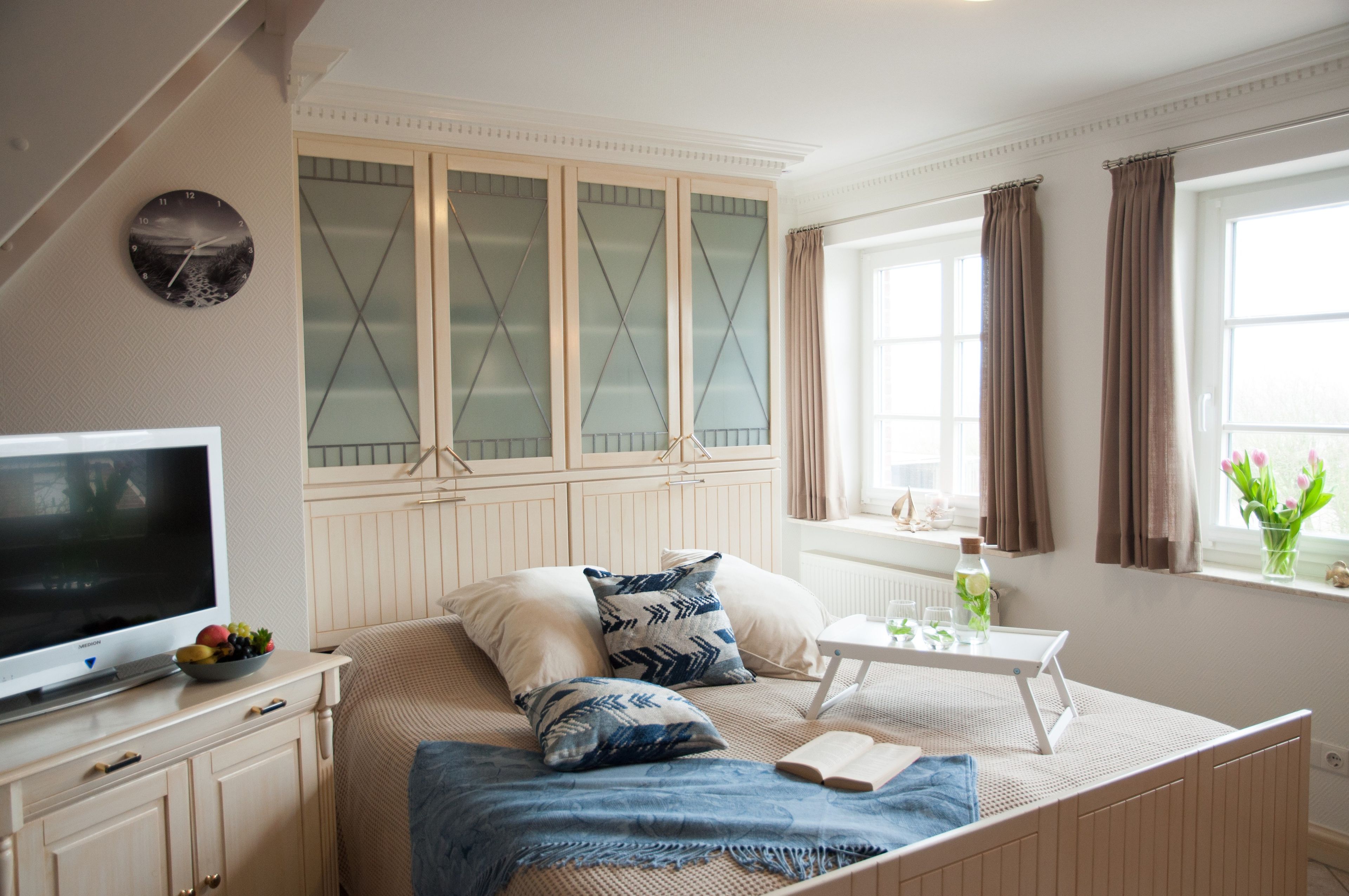 A bedroom with a bed, a television, a window with curtains, and a cabinet with glass doors.