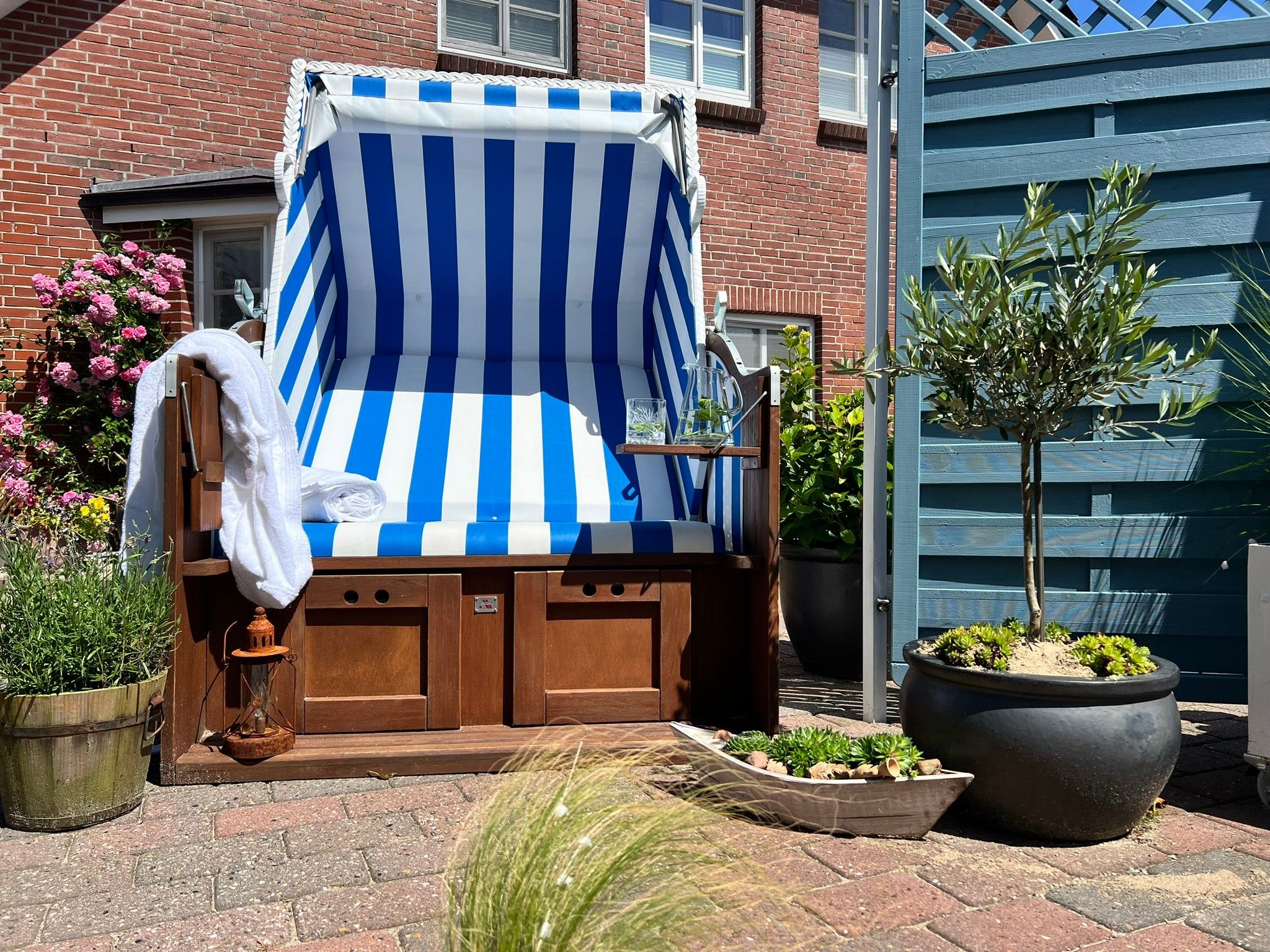 Une chaise de plage avec un parasol à rayures, un banc en bois et des plantes en pot.