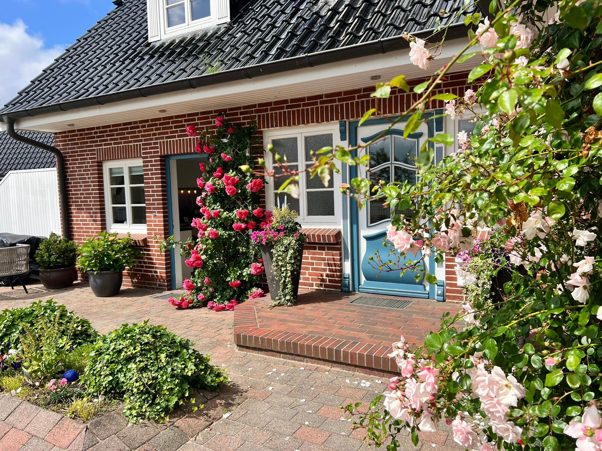 A brick house with a tiled roof, a front door, and a small garden with various plants and flowers.