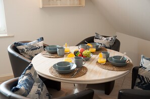 Una mesa de comedor redonda con fuentes, platos y cubiertos grises, rodeada de sillas con cojines de estampado azul.