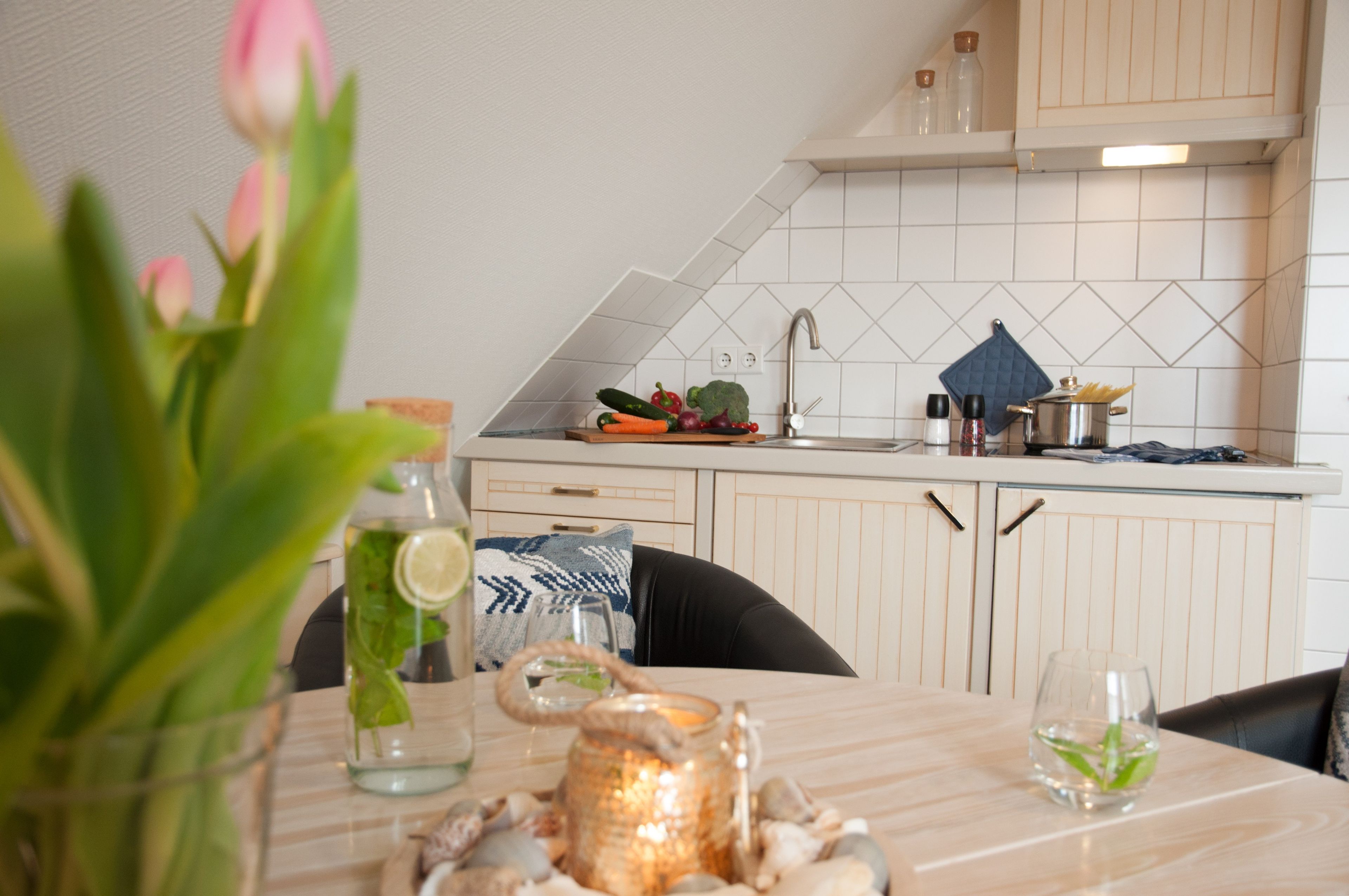 Une cuisine avec des meubles blancs, un pare-feu en carrelage et une table à manger agrémentée d’un vase de fleurs.