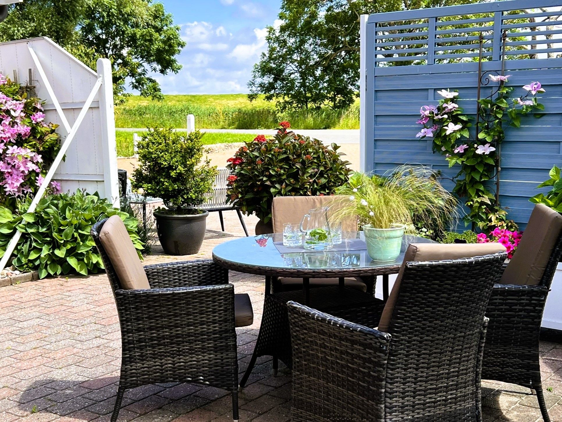 Une terrasse extérieure aménagée avec des meubles en osier, une table ronde en verre et des plantes en pot.