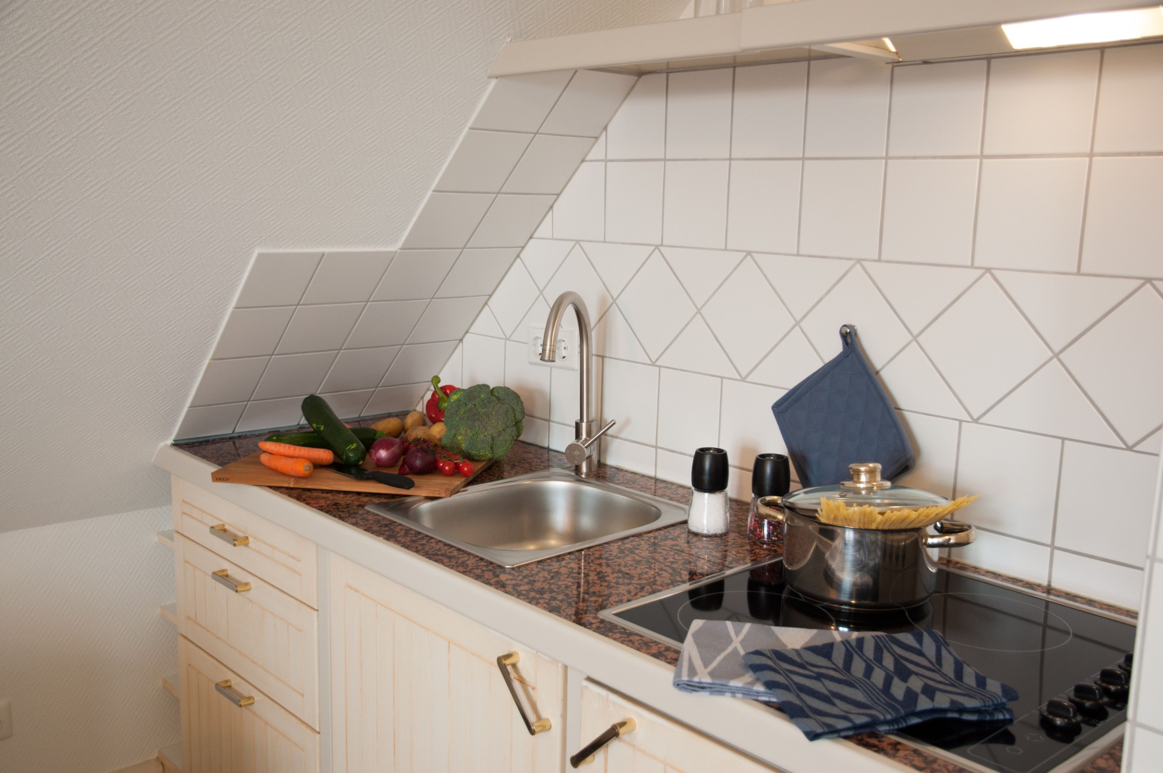 A kitchen with a sink, countertop, stove, and a variety of vegetables.