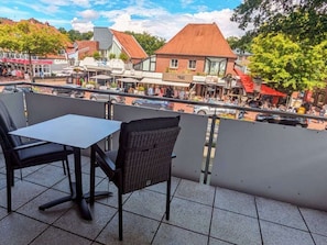 Ein Sitzbereich im Freien mit Tisch und Stühlen, mit Blick auf eine Straße mit Geschäften und einem Gebäude mit rotem Dach.