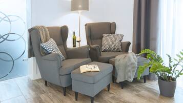 A modern living room with grey sofas, a small ottoman, a floor lamp, and a potted plant.