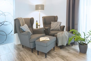 A modern living room with grey sofas, a small ottoman, a floor lamp, and a potted plant.