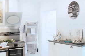 A kitchen with a built-in oven, a stainless steel range hood, a towel rack, and a decorative wall clock.