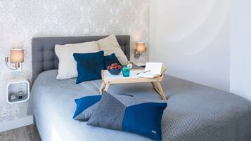 A neatly arranged bedroom with a bed, pillows, bedside lamps, a bedside table with a book and a glass of water, and a wall with a patterned wallpaper.
