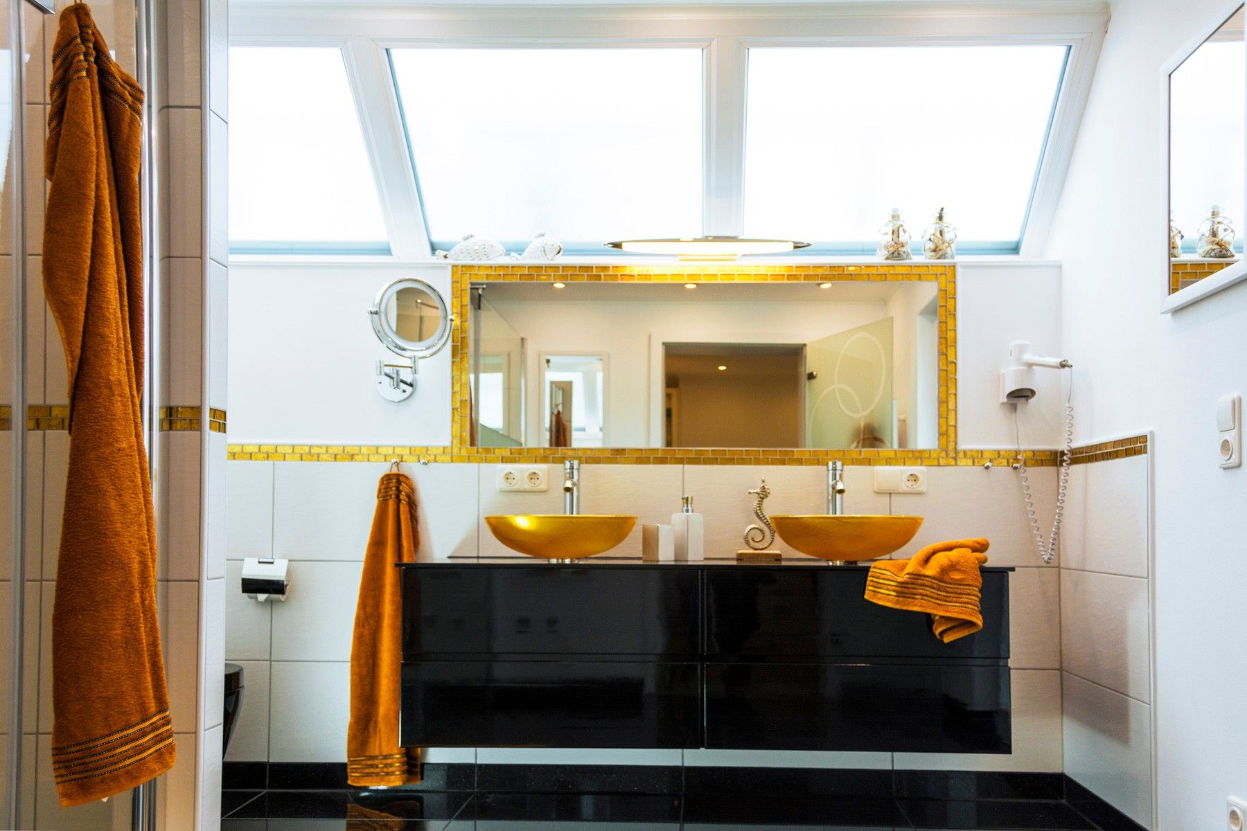 A modern bathroom with a skylight, two sinks with gold bowls, a large mirror, and a towel rack.