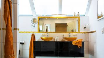 A modern bathroom with a skylight, two sinks with gold bowls, a large mirror, and a towel rack.