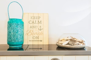 A teal decorative container, a wooden sign with 'KEEP CALM AND ON' text, and a glass bowl with wood shavings on a countertop.