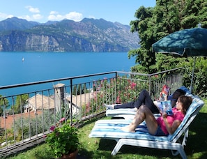 A balcony with a view of a lake and mountains, two lounge chairs, and a potted plant. - Villa Stellina No. 2 (Malcesine)