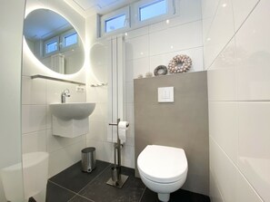 A modern bathroom with a white sink, toilet, and bidet. There is a mirror above the sink and a shower area with a glass door. - Zo10 Holiday Home Zoutelande (Zoutelande)