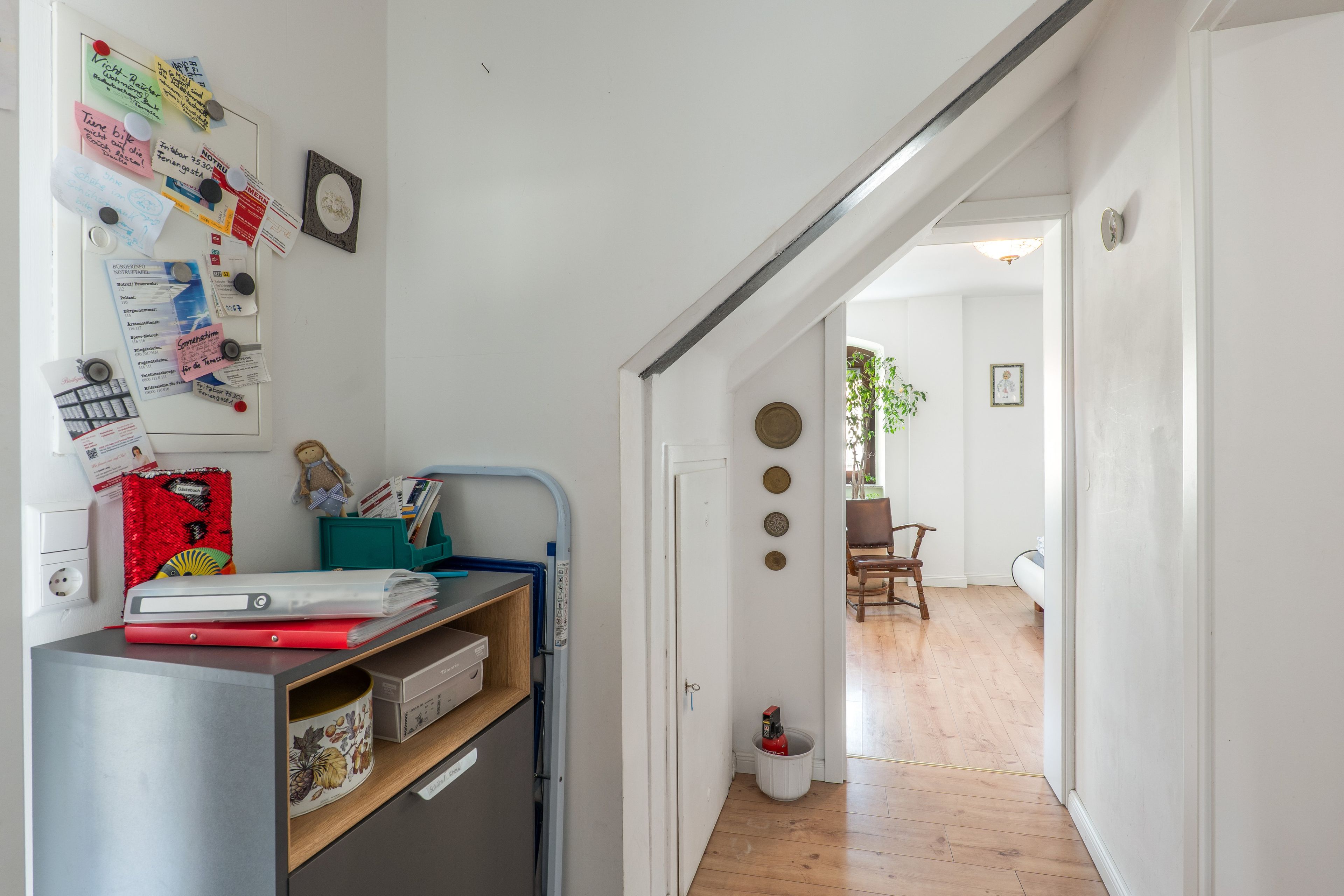 A hallway with a desk cluttered with papers, a small chair, and a red fire extinguisher.