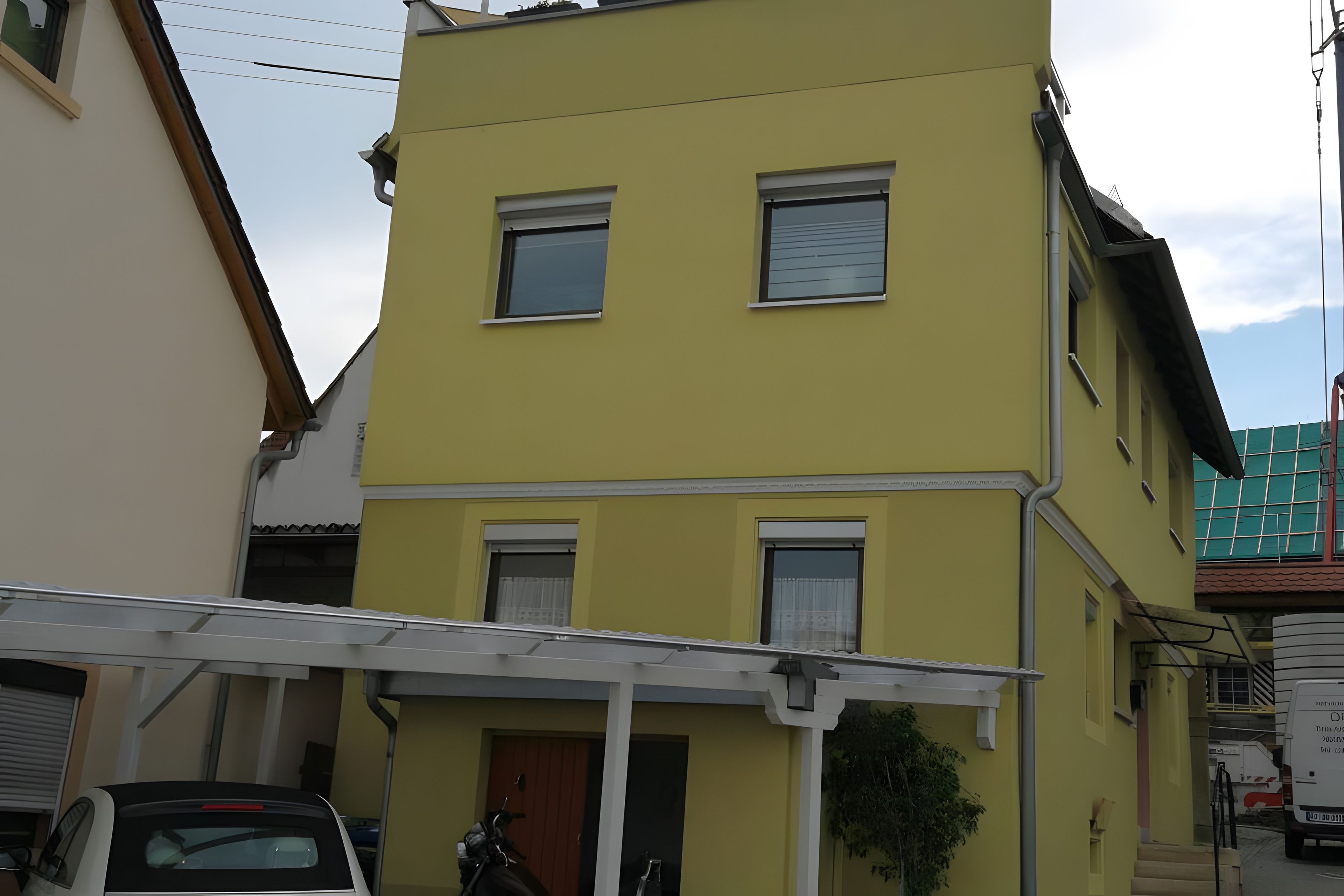 Un edificio a due piani con facciata gialla, un'area di parcheggio coperta e un'auto parcheggiata.
