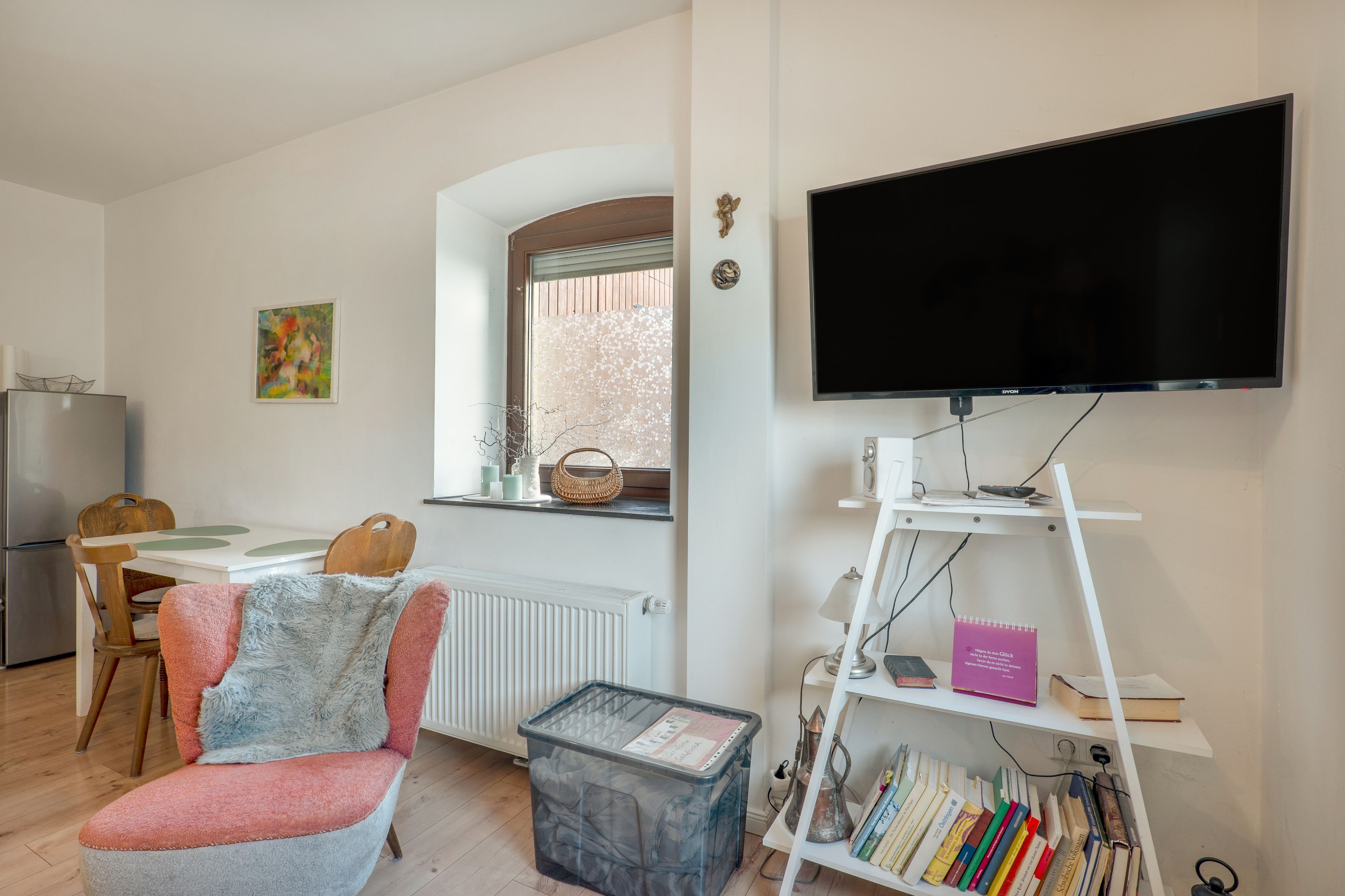 Un salon comprenant un téléviseur, une bibliothèque, un coin repas avec une table et des chaises, et un radiateur.