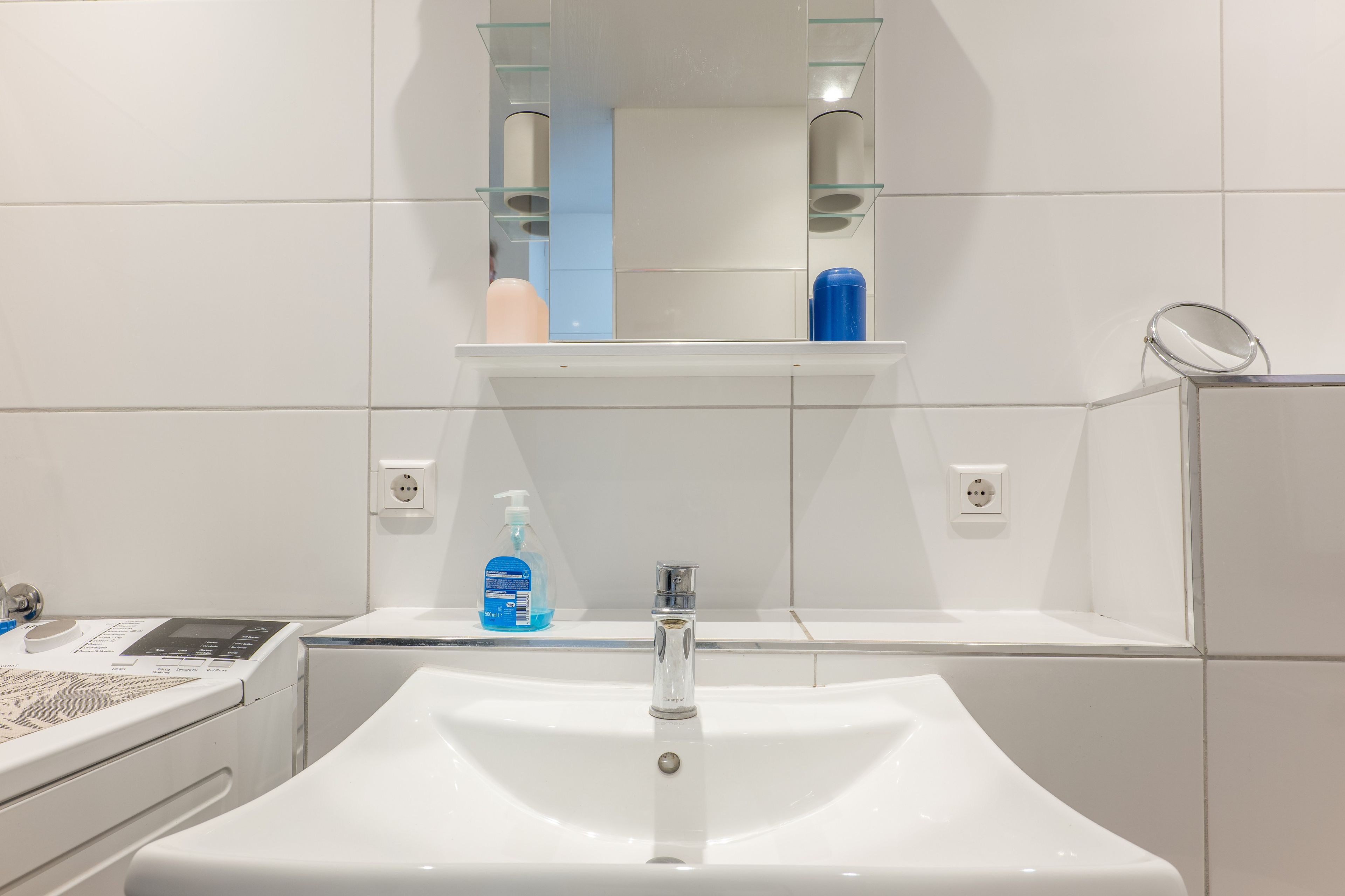 A bathroom with a white sink, a mirror, and a shelf with toiletries.