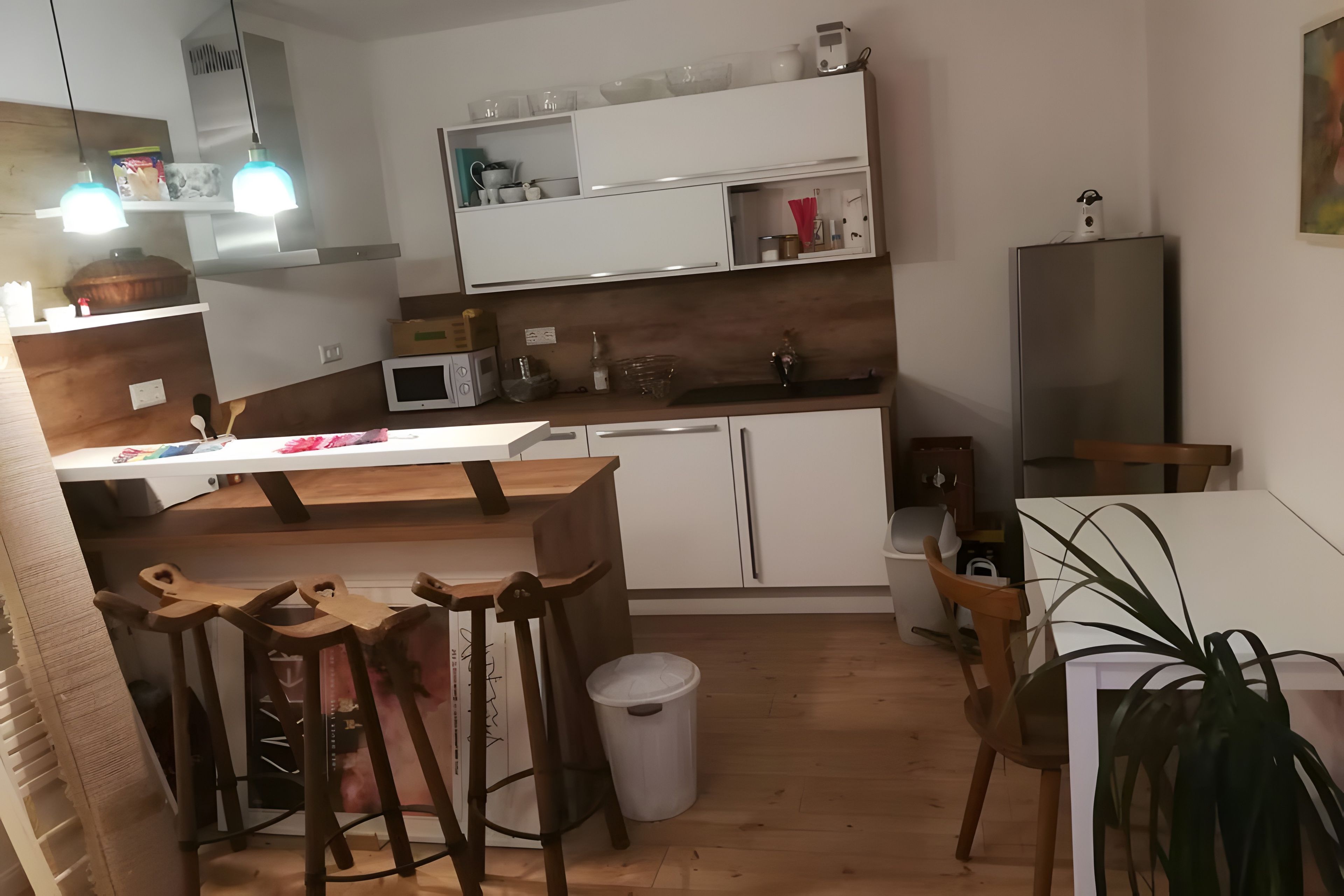 Una cucina compatta con mobili bianchi, un forno a microonde, un lavello e un'area pranzo con sedie in legno.