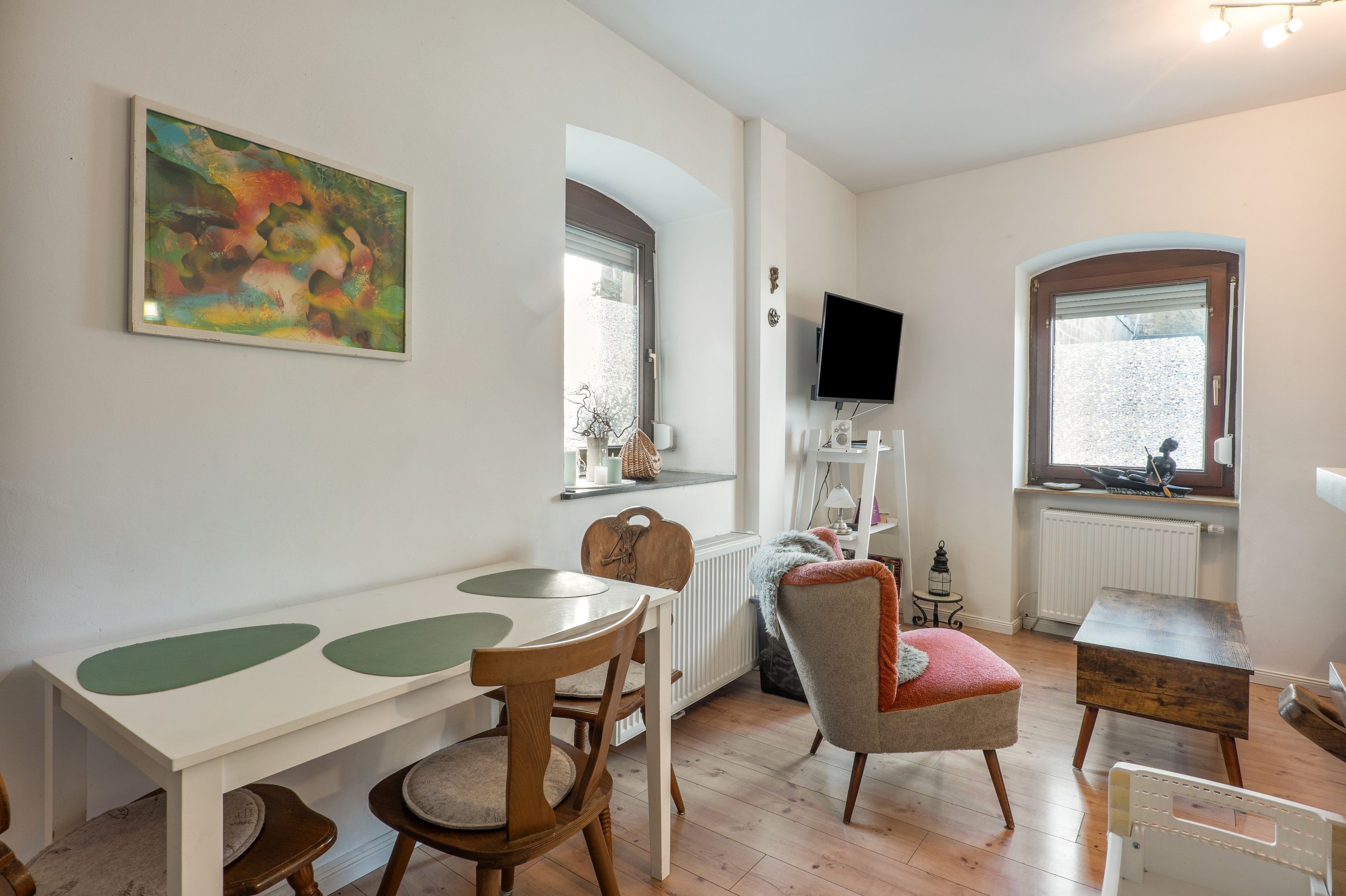 A room with a dining table, chairs, a television, and windows with blinds.
