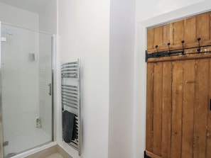 A bathroom with a glass shower enclosure, a towel rack, and a wooden wardrobe. - 8 Douglas Place (Isle of Arran)