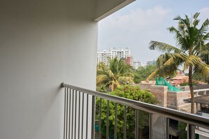 Een balkon met metalen hekwerk met uitzicht op een woongebied met palmbomen en gebouwen.