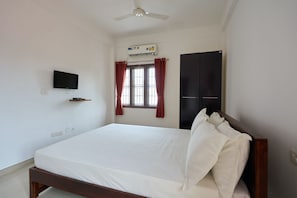 A bedroom with a bed, a television, an air conditioning unit, a window with curtains, and a wardrobe.