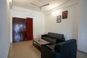 Ein Wohnzimmer mit Sofa, Couchtisch, Deckenventilator, einer Tür mit Vorhängen und zwei gerahmten Bildern an der Wand.