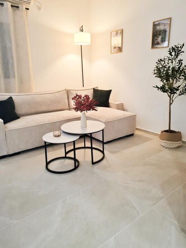 A living room with a beige sofa, a round coffee table with a vase, a floor lamp, and a potted plant. - Vrbo Property (Tribunj)