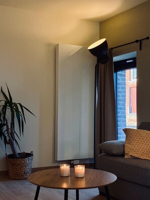 Un salon moderne avec une table ronde en bois, deux bougies, une plante en pot et un canapé agrémenté de coussins.
