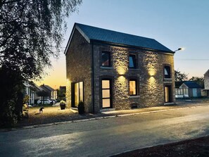 A two-story stone building with a sloped roof, large windows, and exterior lighting. - La Petite Maison de Frisée - Charm in the Condroz (Hamois)