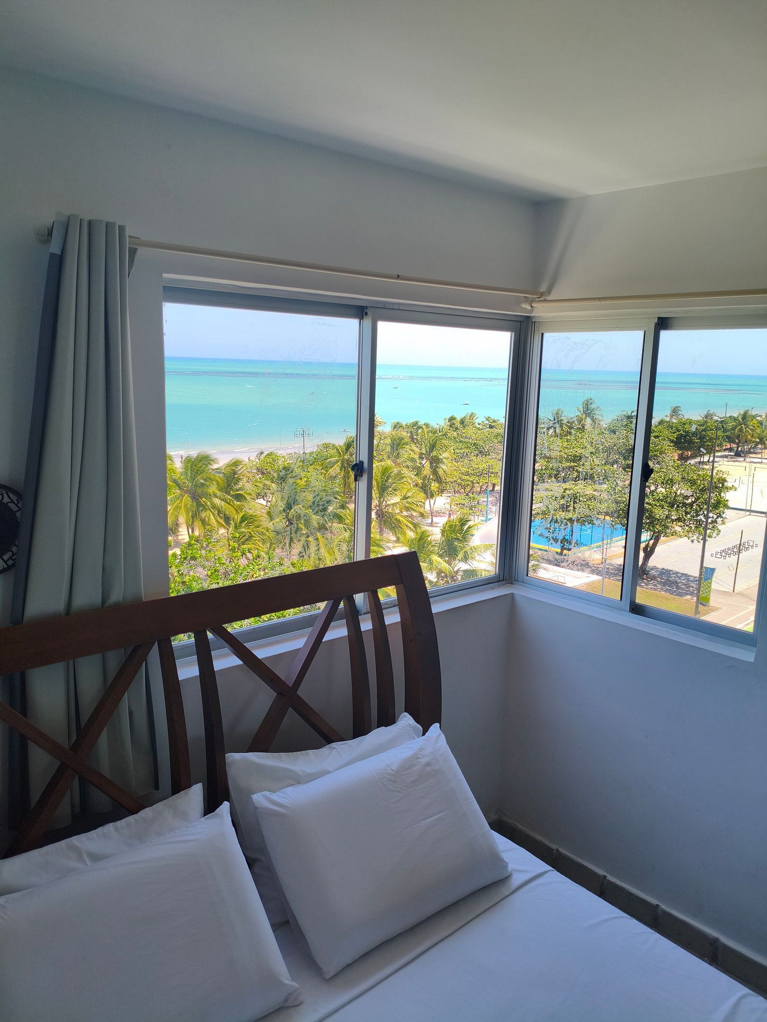 A hotel room with a bed, a large window, and a view of the beach.