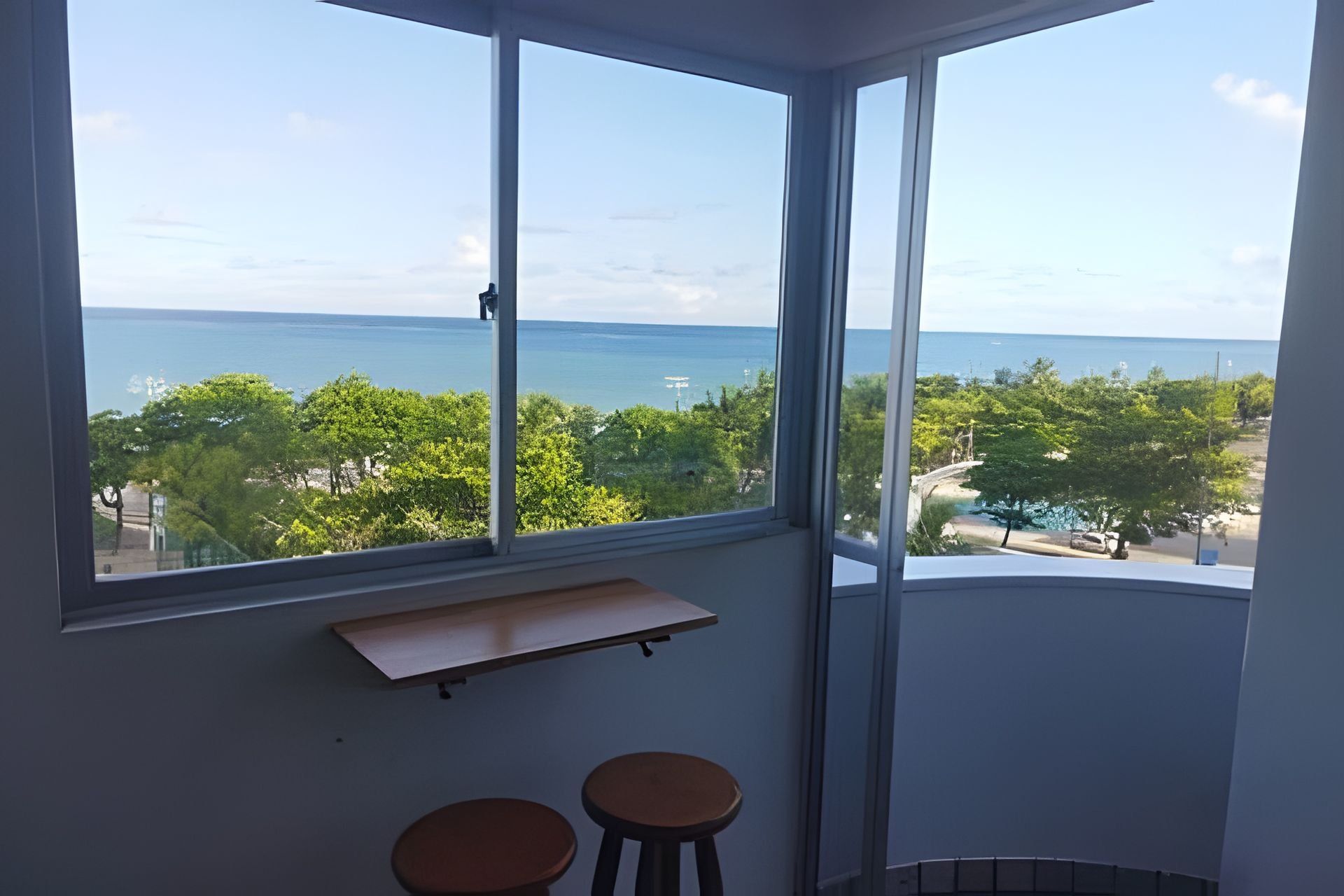 A room with a large window offering a view of the sea and greenery.