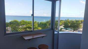 A room with a large window offering a view of the sea and greenery.