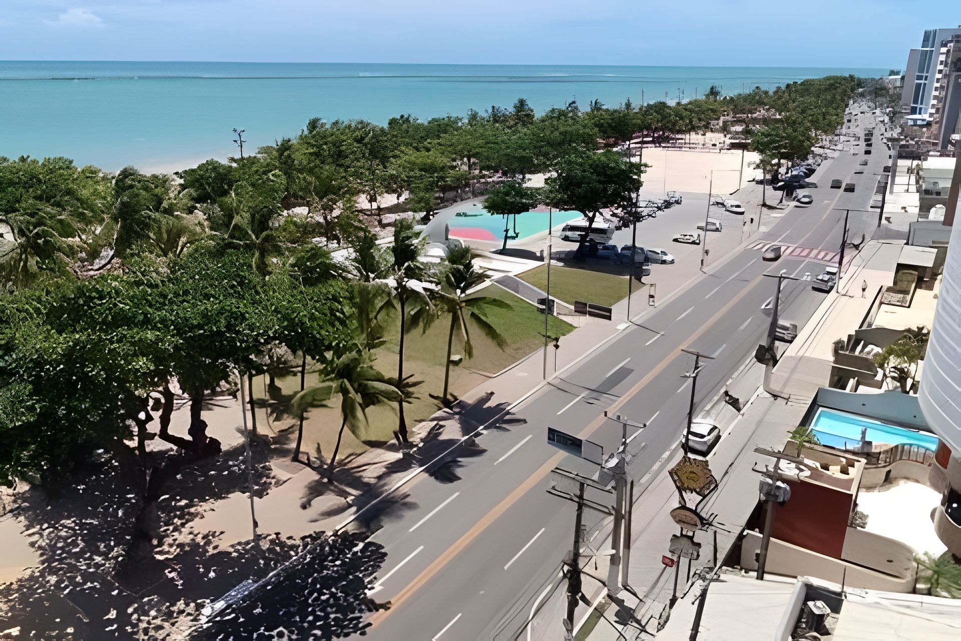 Un paysage urbain côtier avec une large route, des palmiers et une plage en arrière-plan.