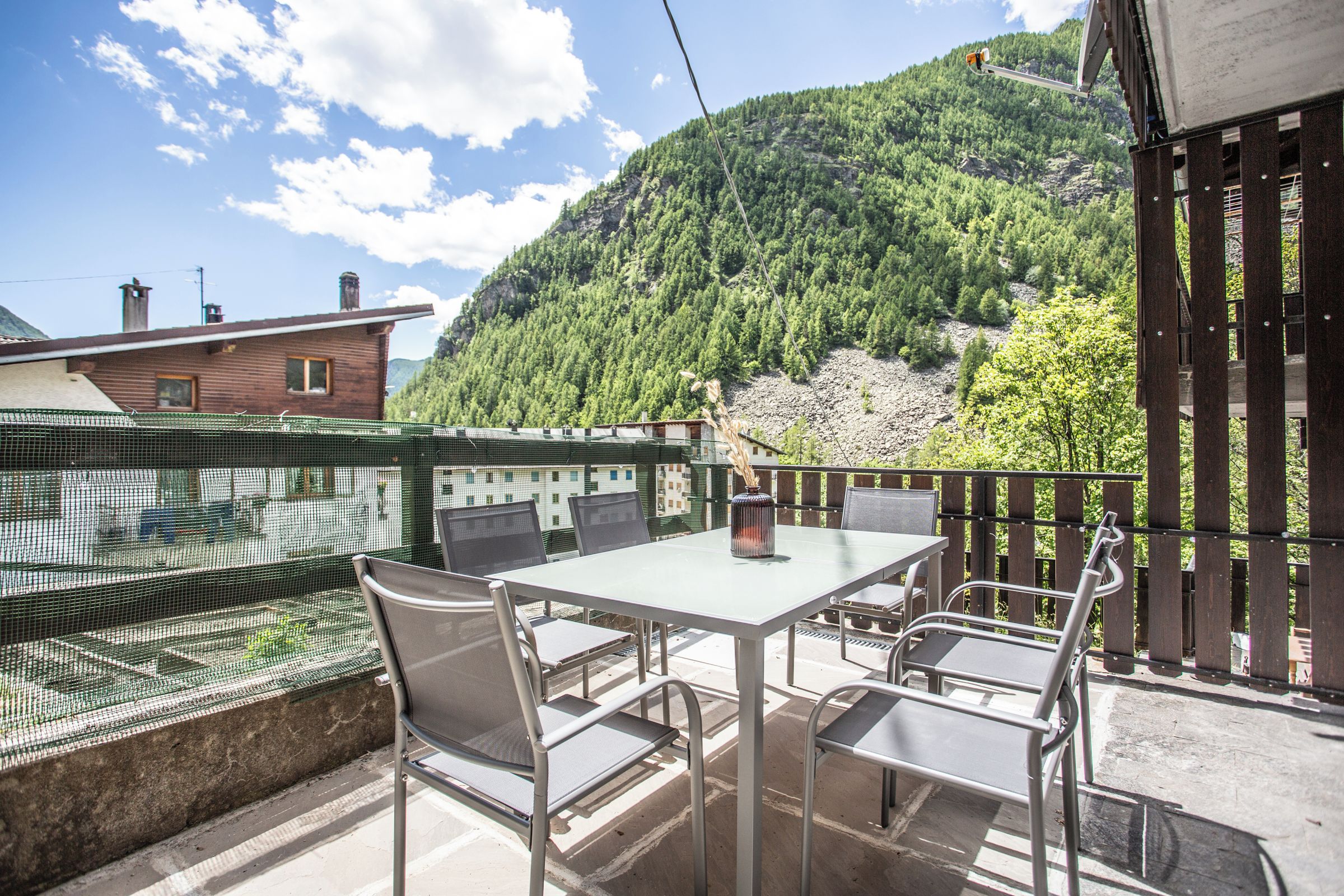 Eine Terrasse mit Tisch und Stühlen, mit Blick auf eine gebirgige Landschaft mit dichtem Grün.