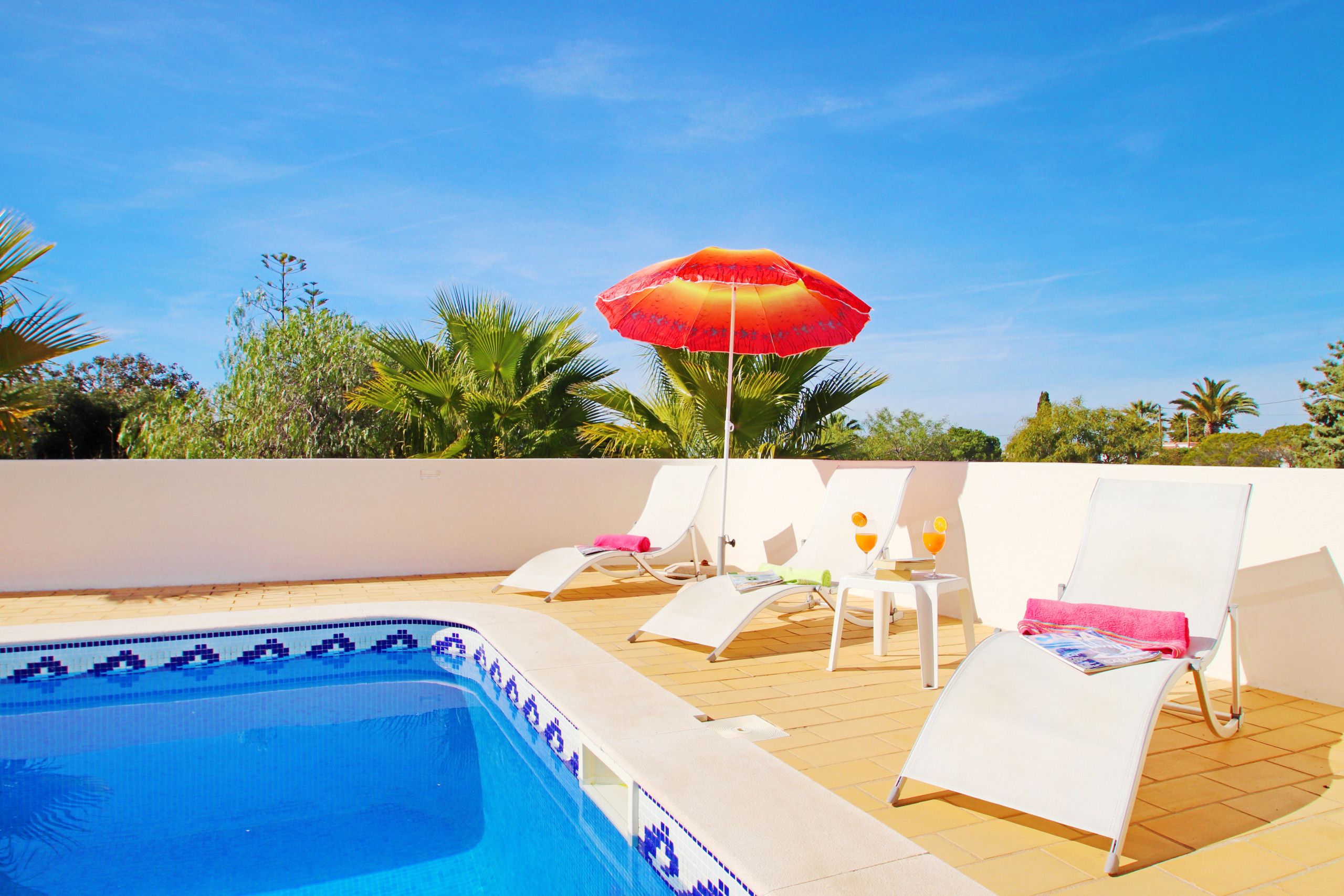 Un espace piscine avec des chaises longues et un parasol.