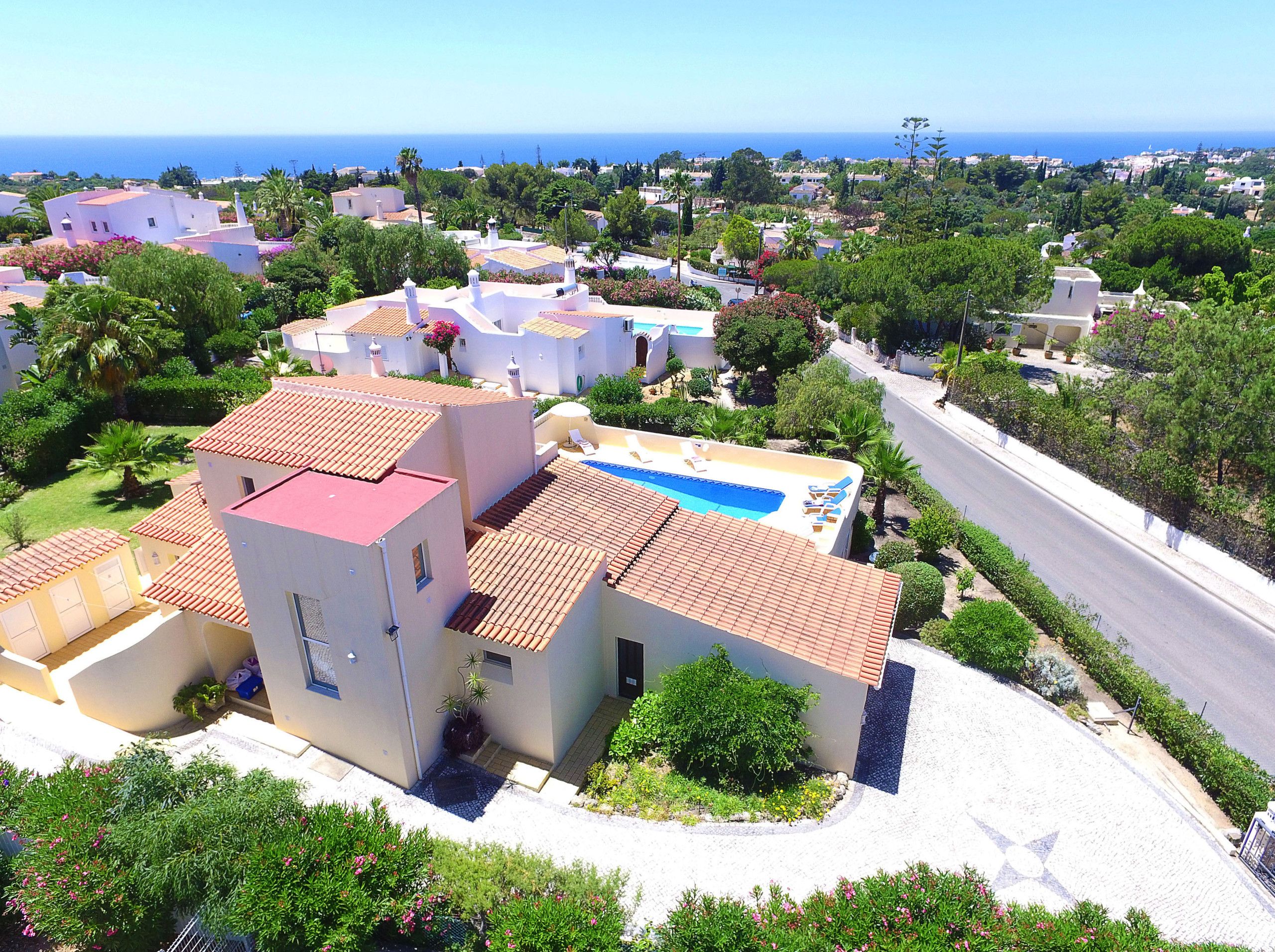 A residential area with a swimming pool, white buildings, and a view of the sea.