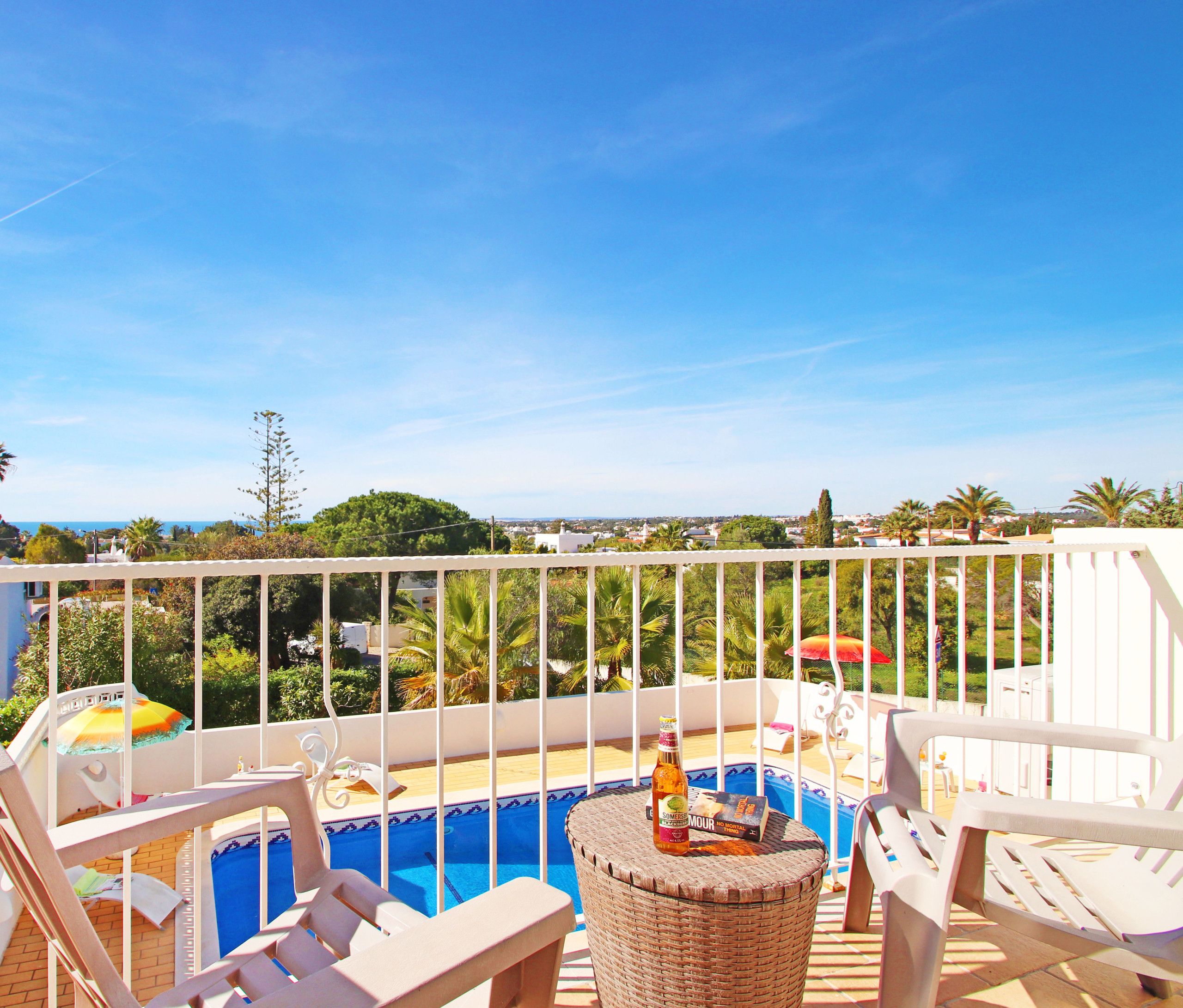 A balcony with a pool, lounge chairs, and a view of the surrounding landscape.