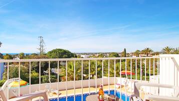A balcony with a pool, lounge chairs, and a view of the surrounding landscape.