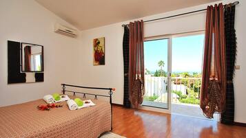 A bedroom with a bed, a painting, an air conditioner, and a view through the window.