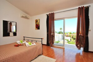A bedroom with a bed, a painting, an air conditioner, and a view through the window.