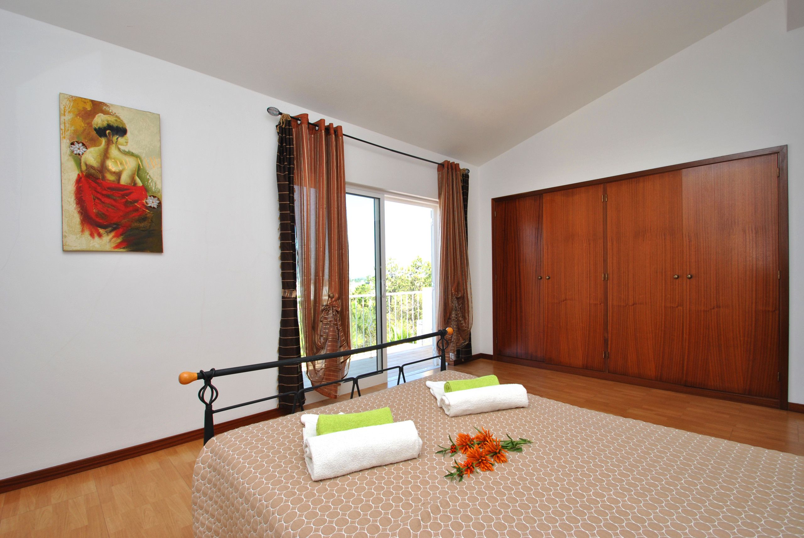 A bedroom with a bed, a large wardrobe, a painting on the wall, and a window with curtains.