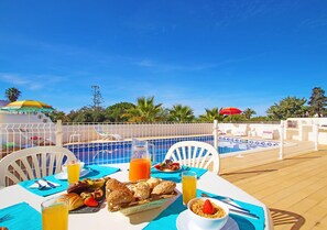 Area ristorazione a bordo piscina con tavolo apparecchiato per la colazione, inclusi pane, frutta e bevande.