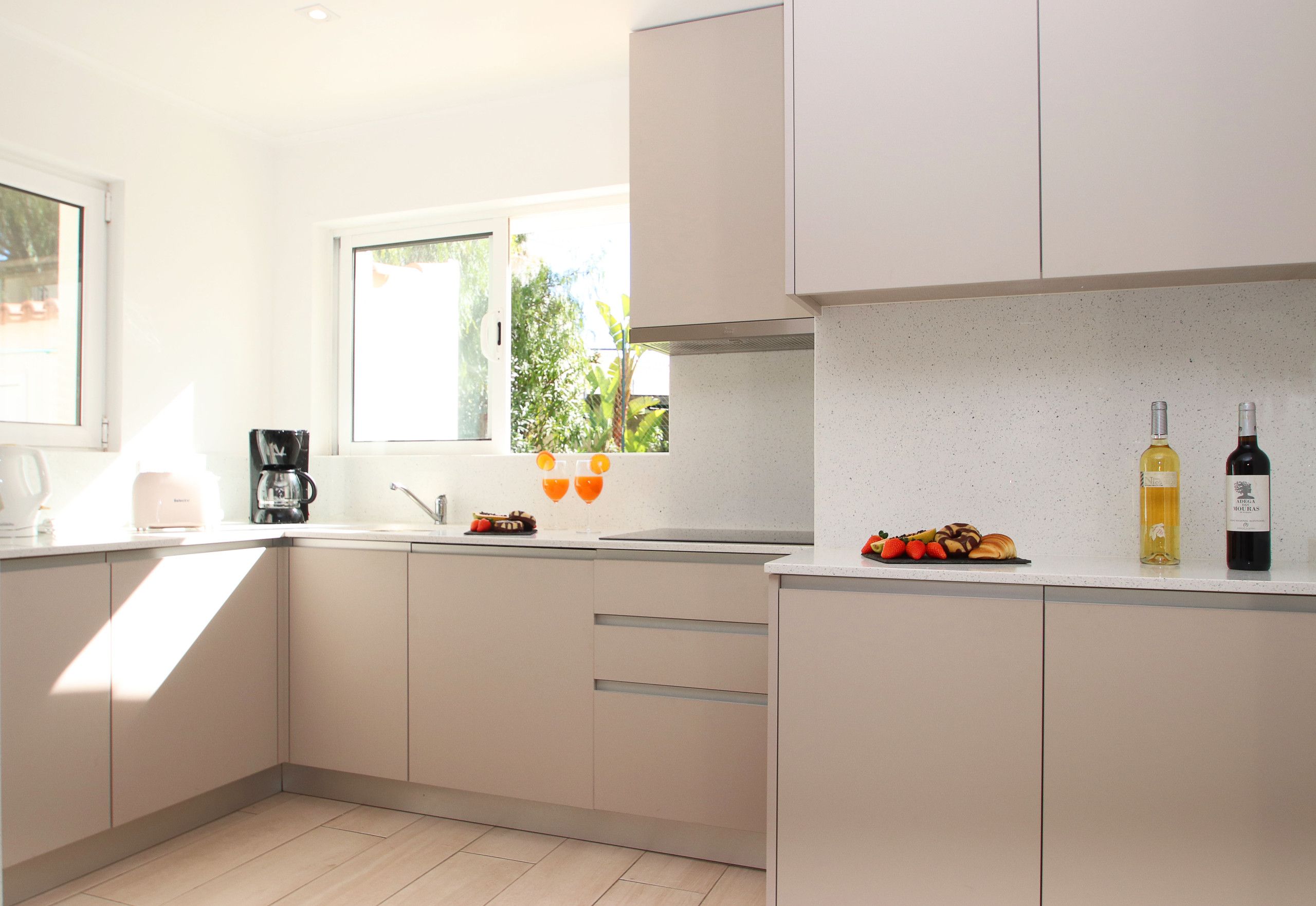 A modern kitchen with a window, a coffee maker, and two bottles of wine on the counter.