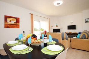 Un coin repas avec une table dressée pour quatre personnes, un téléviseur et un canapé en arrière-plan.